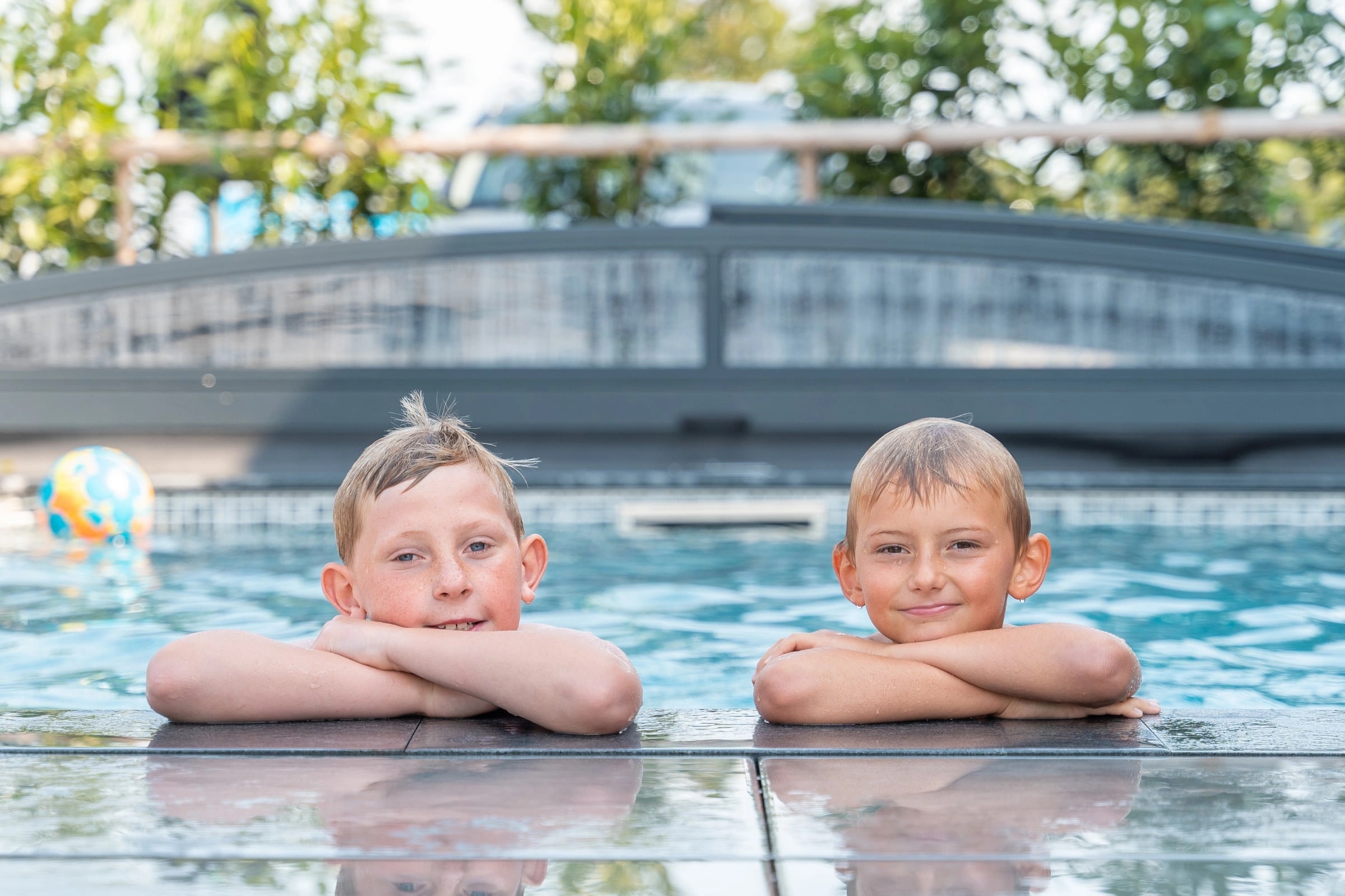 Två pojkar som vilar armarna på poolkanten och tittar in i kameran