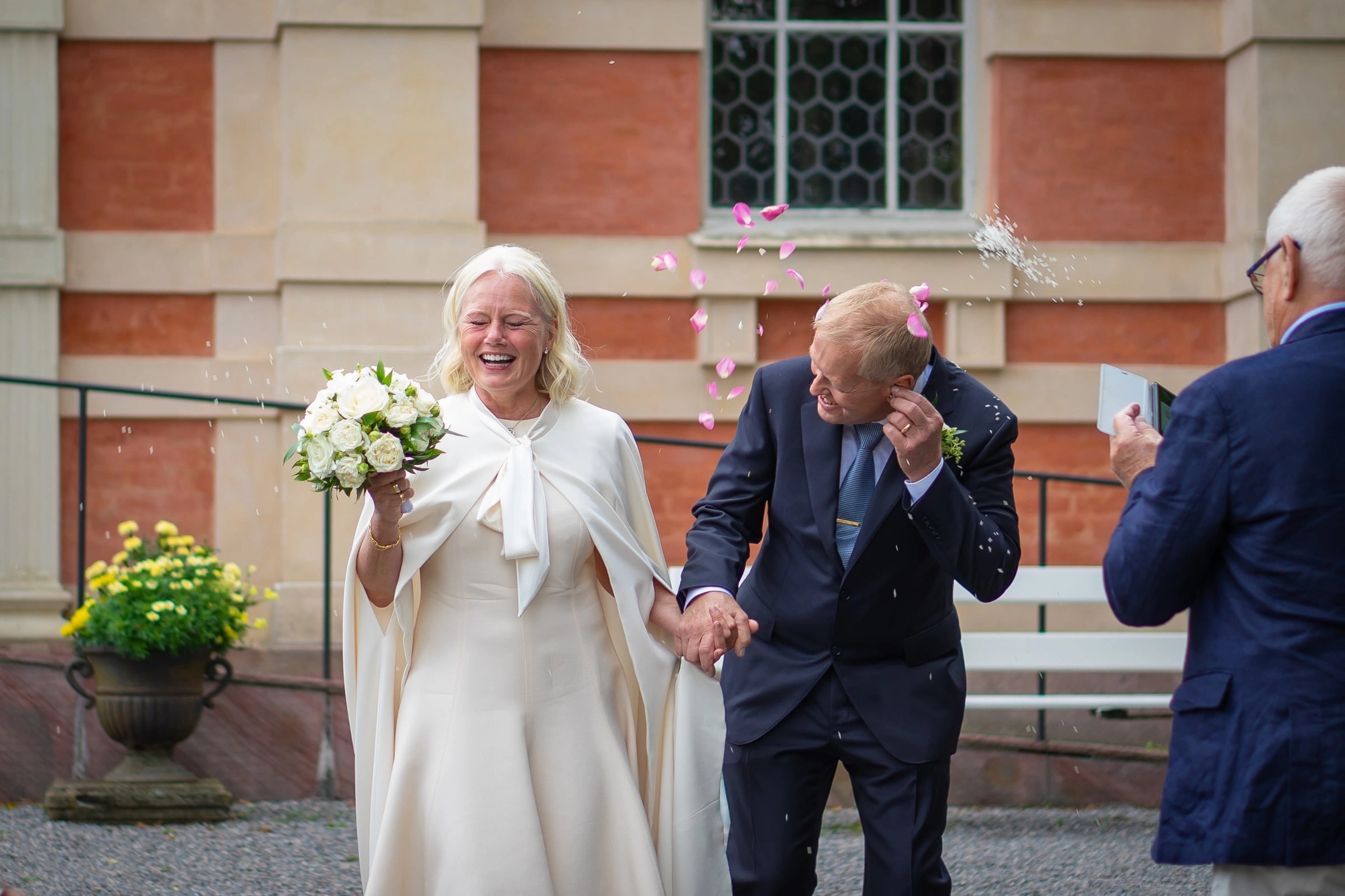 Nygift par som möts av risregn utanför kyrkan, bruden skrattar med brudbuketten i handen